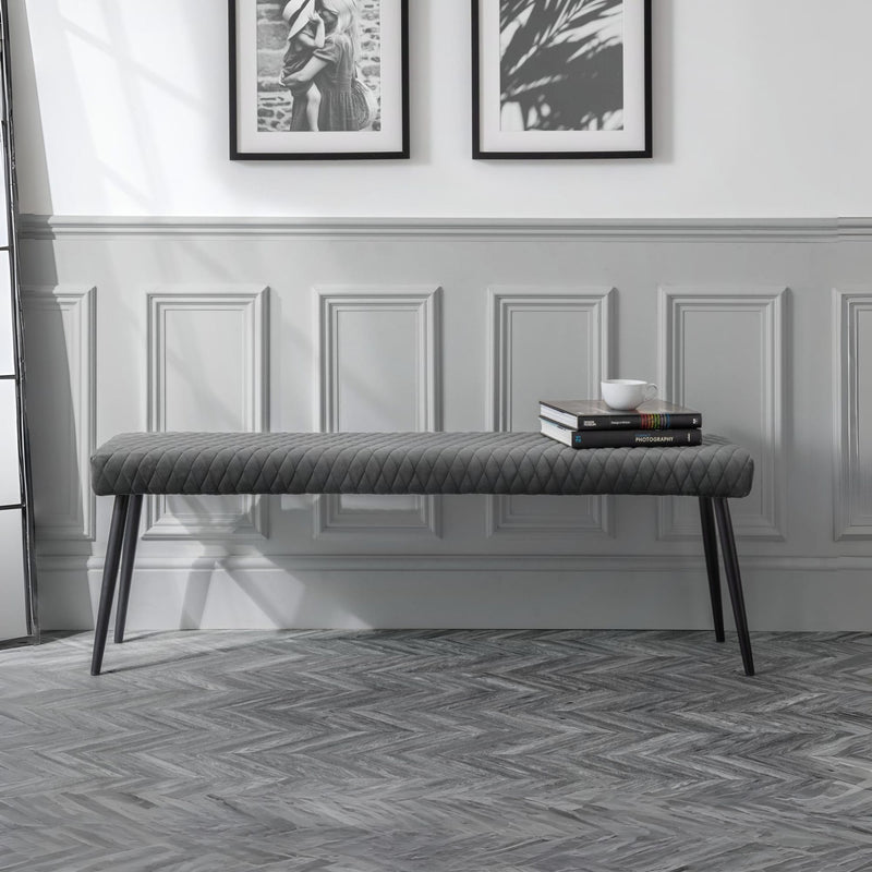 Gray upholstered bench in a room with framed pictures on the wall.