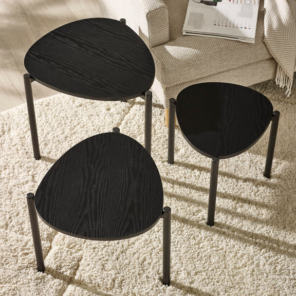 Three black stools on a beige carpet with a light-colored sofa in the background.