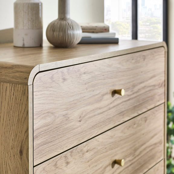 Wooden dresser with two drawers and gold knobs, decorated with vases and books.