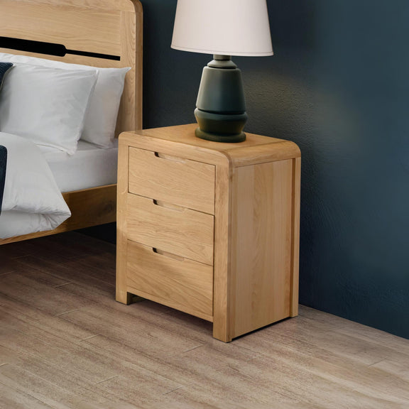 Wooden nightstand with a lamp next to a bed in a bedroom setting.