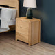 Wooden nightstand with a lamp next to a bed in a bedroom setting.