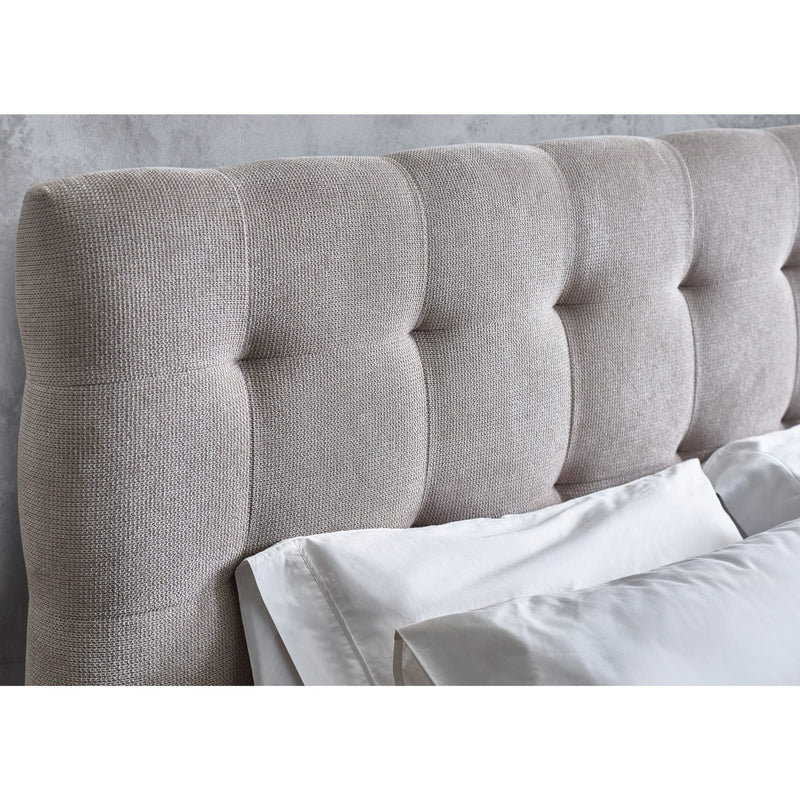 Gray tufted headboard with white bedding against a light gray wall.