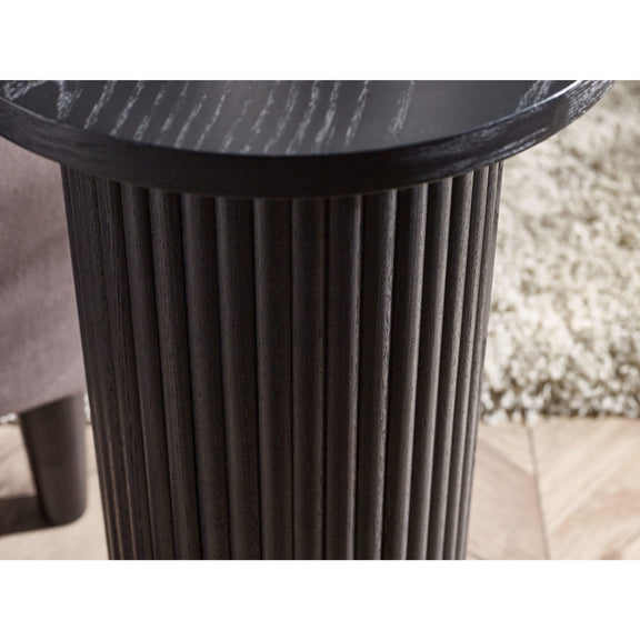 Round black table with ribbed cylindrical base on a blurred outdoor background