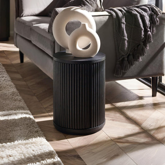 Black side table with a white decorative object in a living room setting