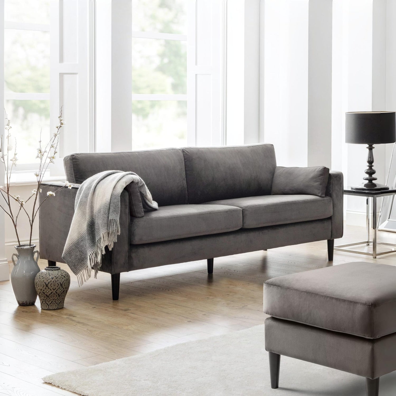 Gray sofa in a living room with large windows and a lamp.