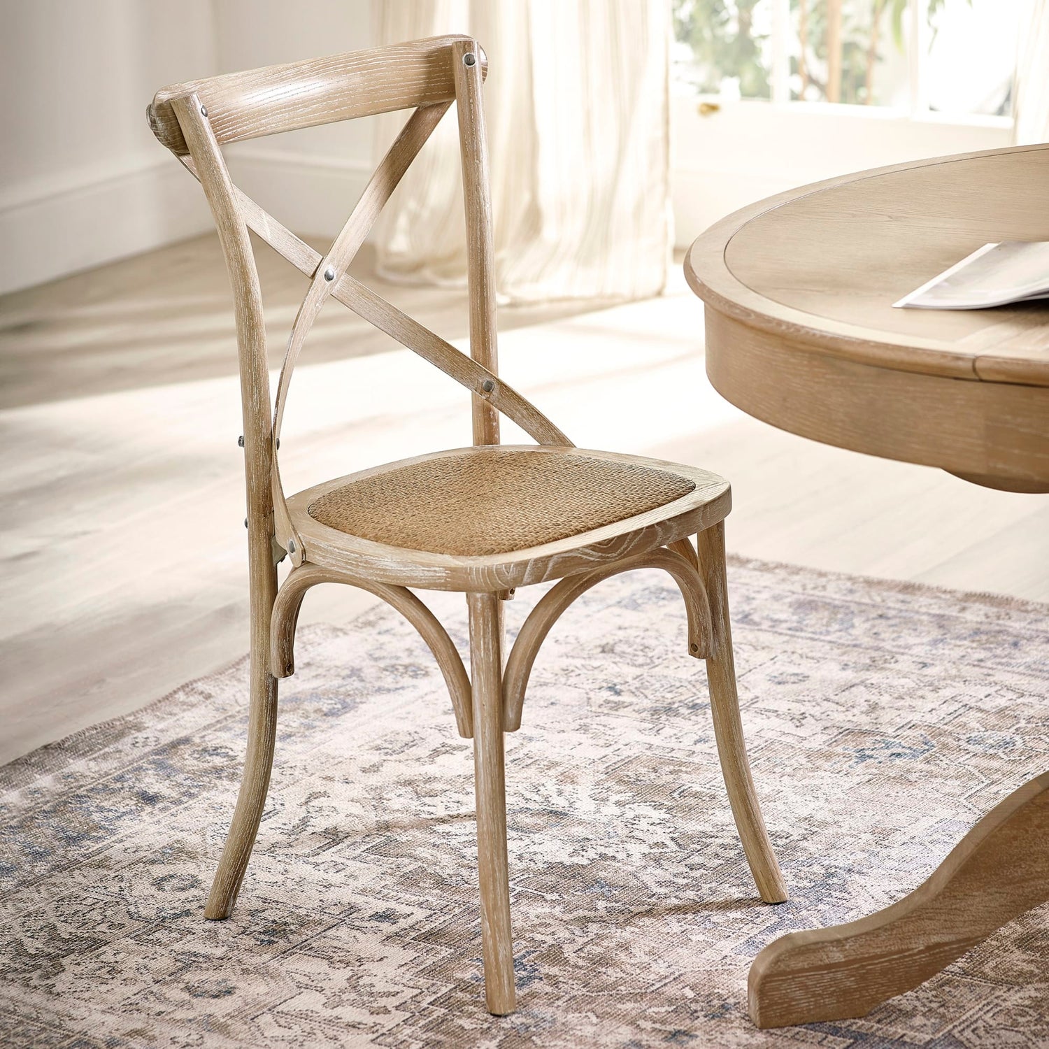 Wooden chair with woven seat next to a round wooden table in a bright room.