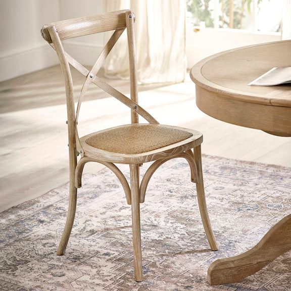 Wooden chair with woven seat next to a round wooden table in a bright room.
