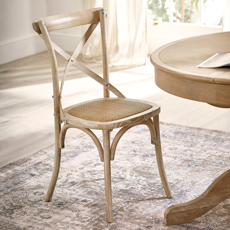 Wooden chair with woven seat next to a round wooden table in a bright room.