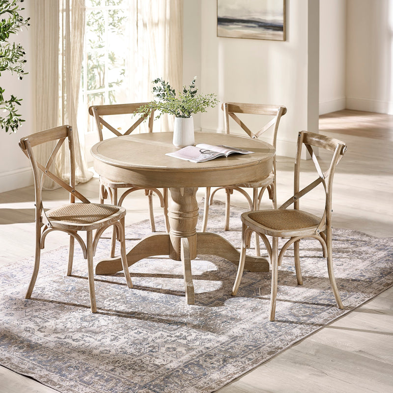 Round wooden dining table with four matching chairs in a bright room.