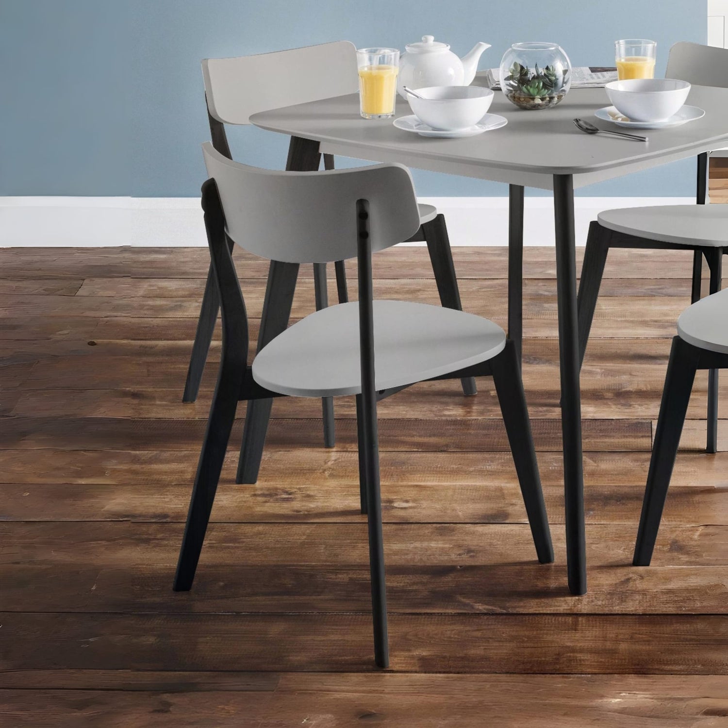 Dining table with chairs on a wooden floor against a light blue wall.