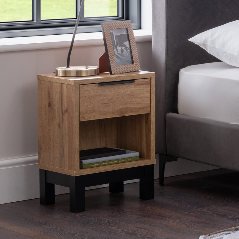 Wooden nightstand with a photo frame and books next to a bed in a bedroom.