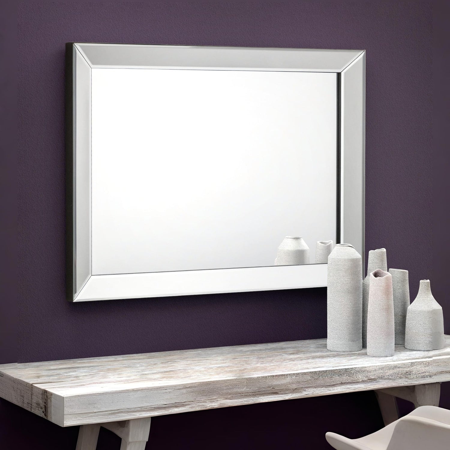 White-framed mirror on a purple wall above a wooden table with decorative vases.