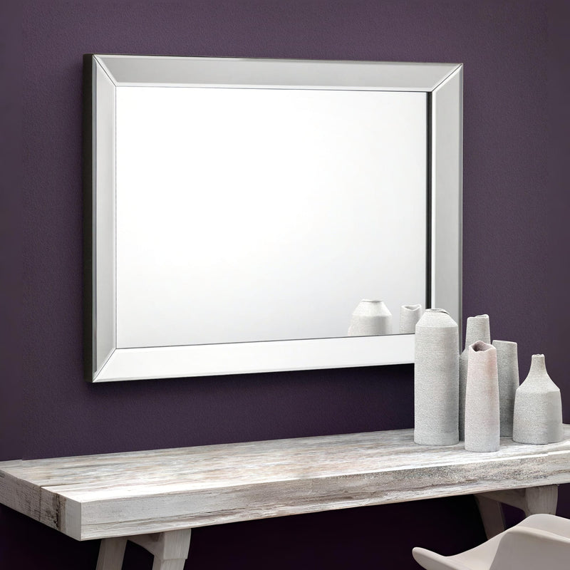 White-framed mirror on a purple wall above a wooden table with decorative vases.