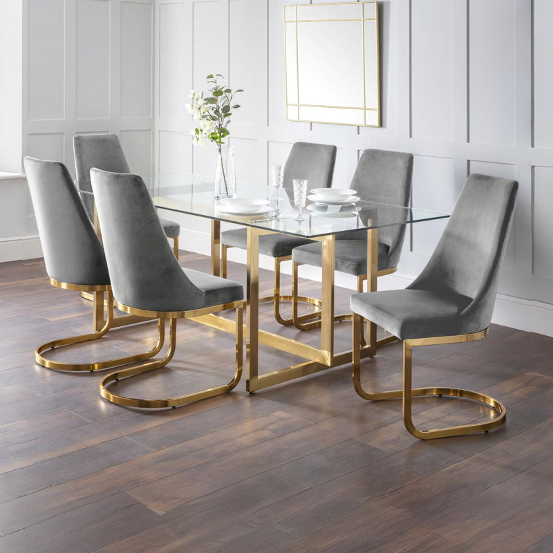 Dining room with a glass table and gray chairs with gold legs.