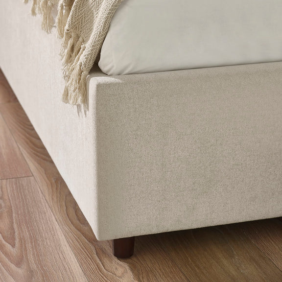 Beige upholstered bed with a wooden footboard on a wooden floor