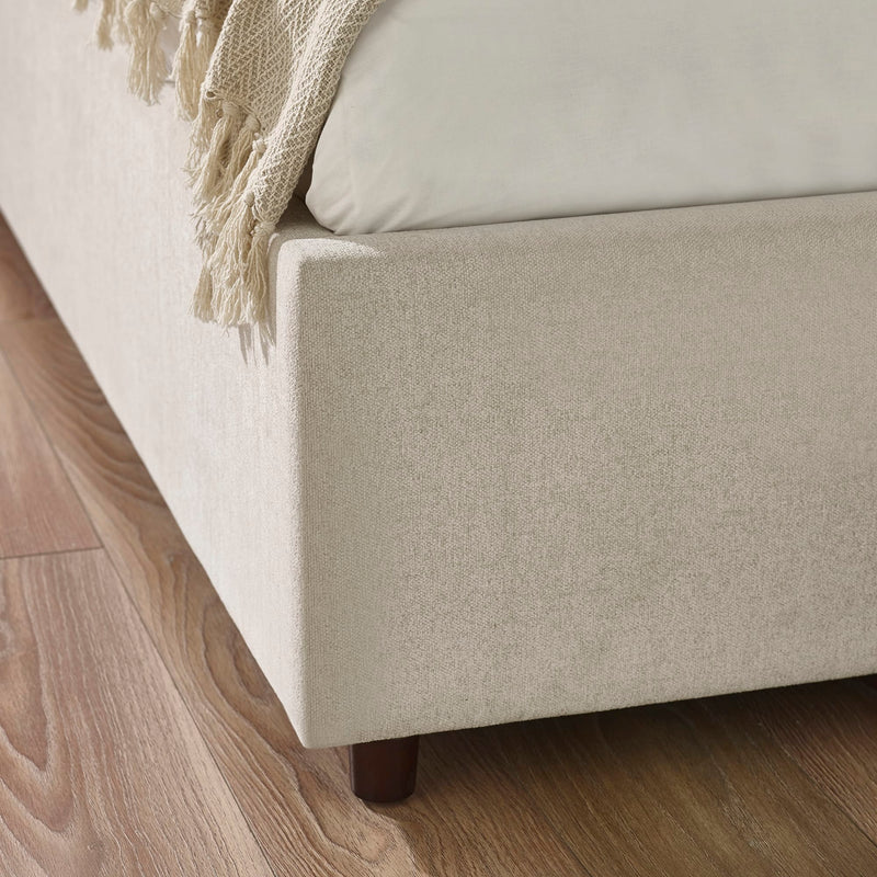 Beige upholstered bed with a wooden footboard on a wooden floor