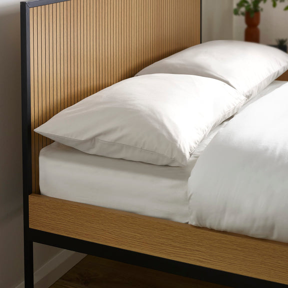 Bed with white bedding and pillows against a wooden headboard.