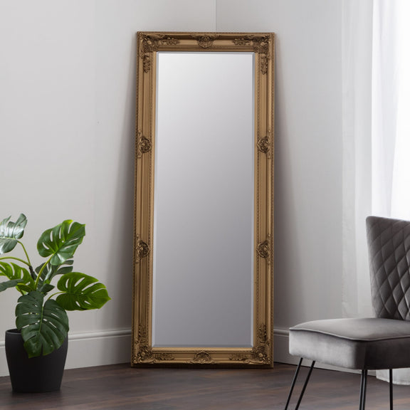 Decorative gold-framed mirror on a wall with a plant and chair in the background