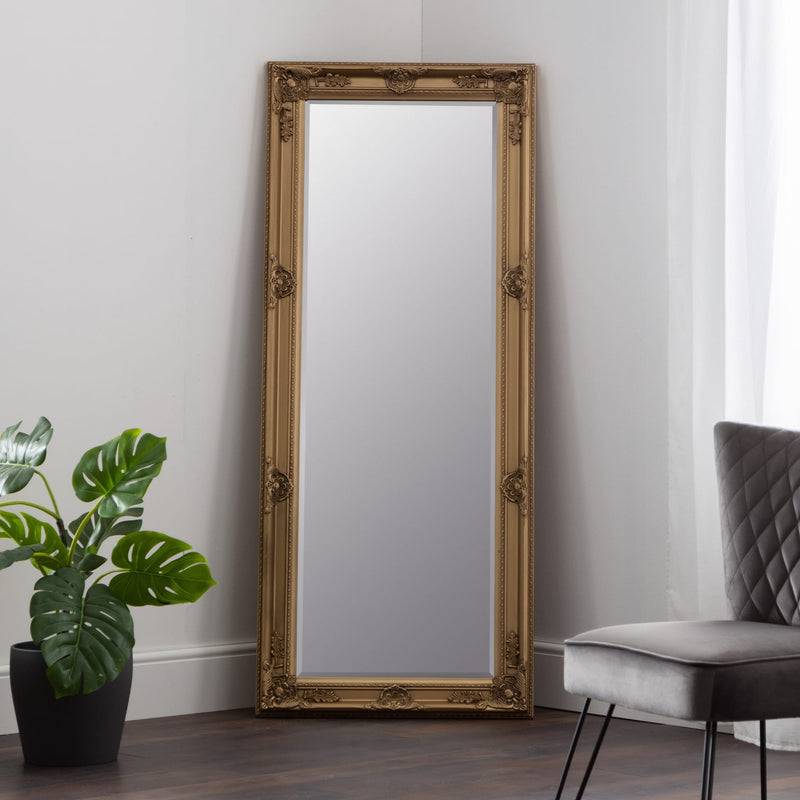 Decorative gold-framed mirror on a wall with a plant and chair in the background