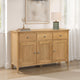 Wooden sideboard with three drawers and two doors in a room with a mirror and lamp.