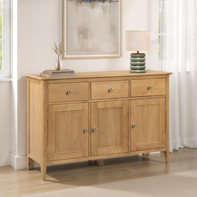 Wooden sideboard with three drawers and two doors in a room with a mirror and lamp.