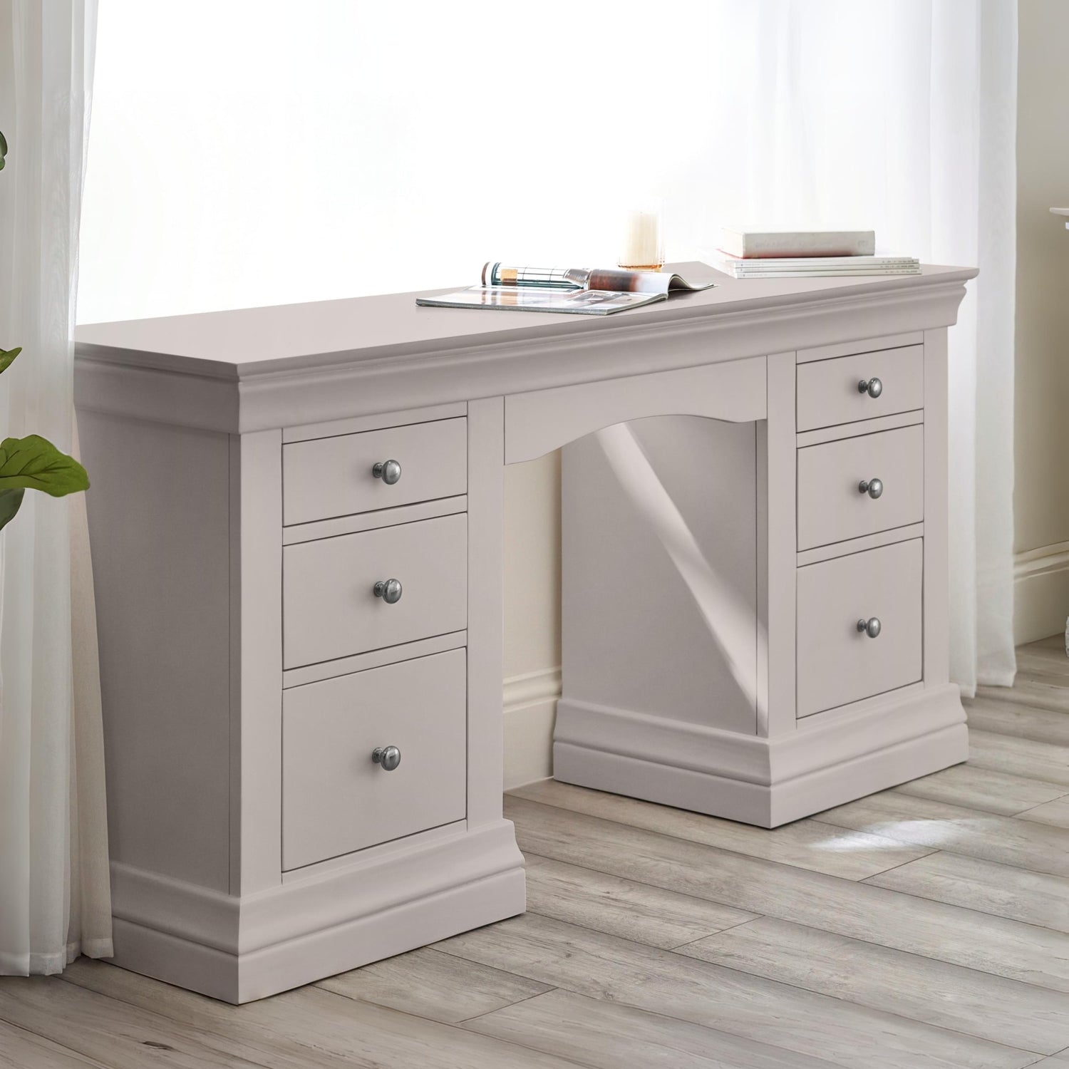 Light gray desk with multiple drawers in a room with white curtains.