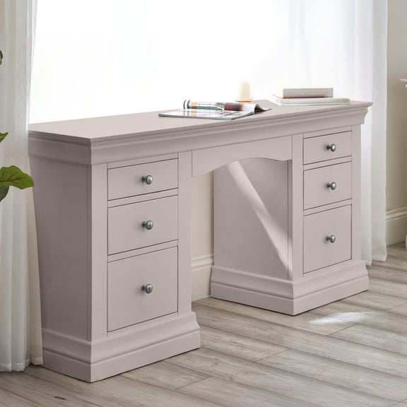 Light gray desk with multiple drawers in a room with white curtains.
