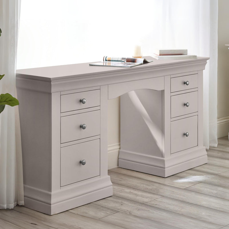 Light gray desk with multiple drawers in a room with white curtains.