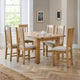 Wooden dining table with six chairs in a well-lit room with large windows.