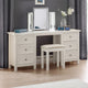White vanity table with mirrors, stool, and decorative items in a room with gray curtains.