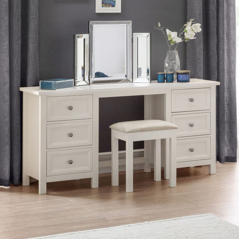White vanity table with mirrors, stool, and decorative items in a room with gray curtains.