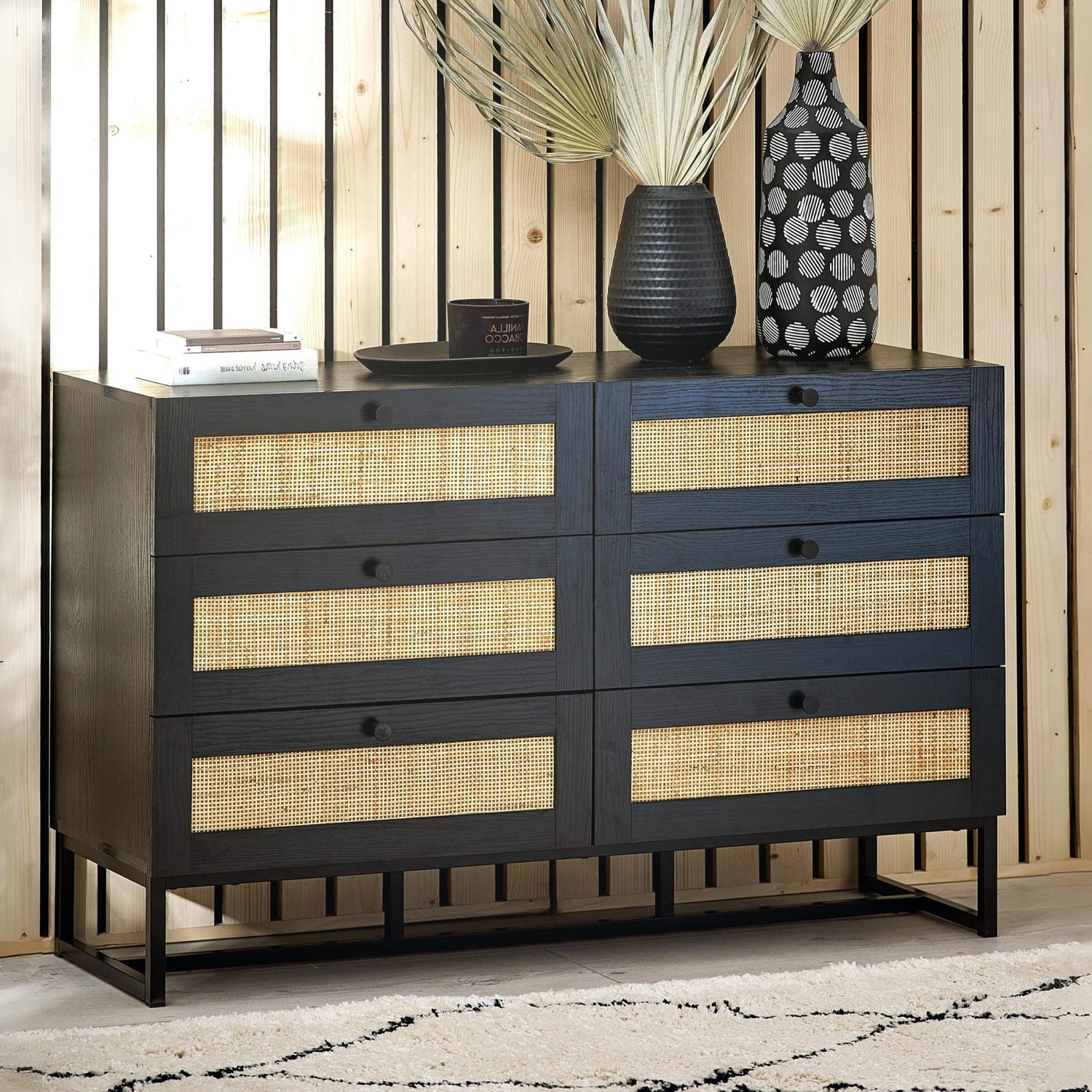 Black dresser with woven drawers against a wooden wall.