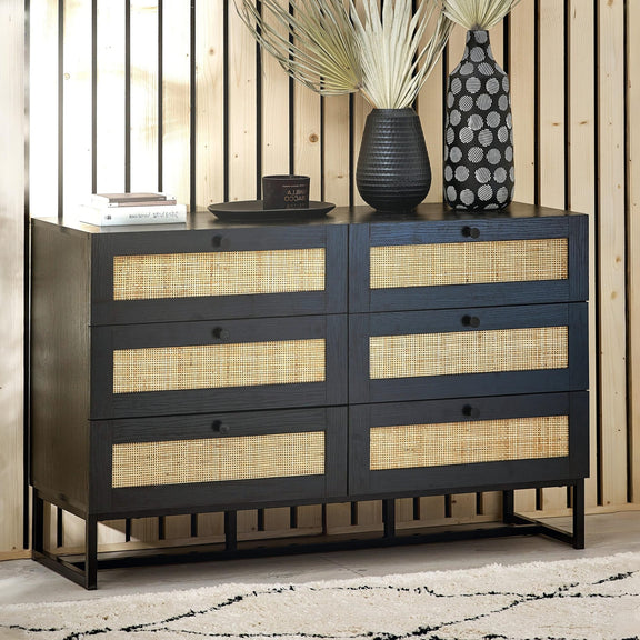 Black dresser with woven drawers against a wooden wall.