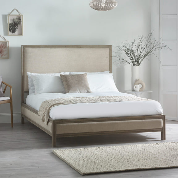 Beige upholstered bed in a bedroom setting with white bedding and decor.