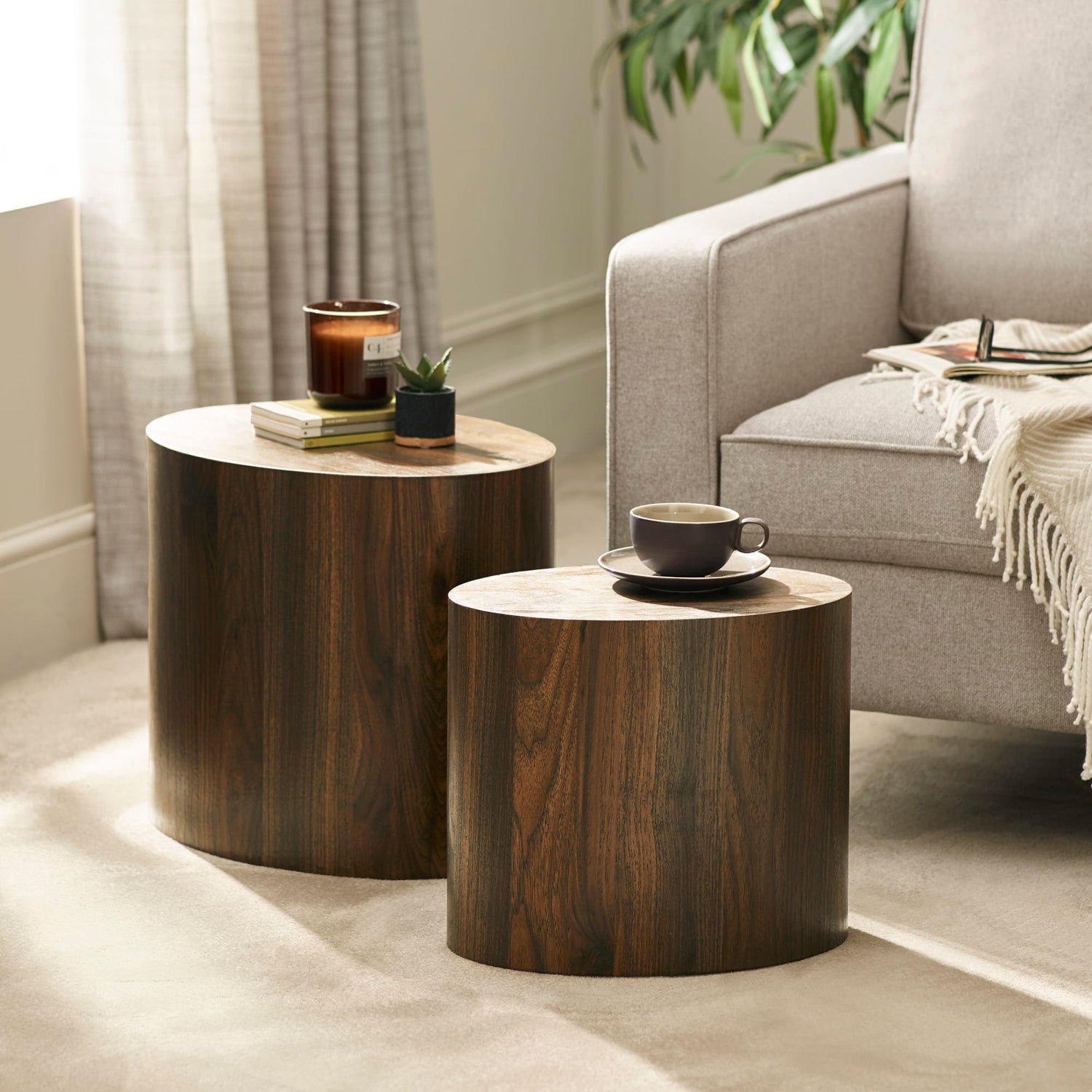 Two wooden side tables with a cup and candle in a living room setting.