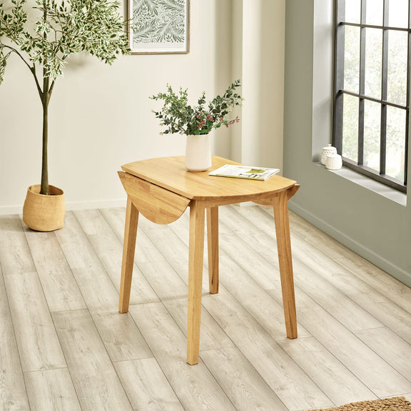 Wooden dining table with a plant and decorative items in a room with light wood flooring and a window.