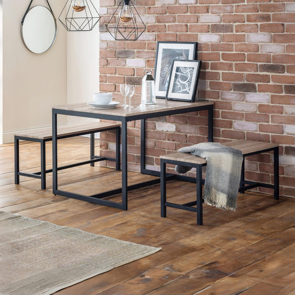 Dining table set with benches against a brick wall.