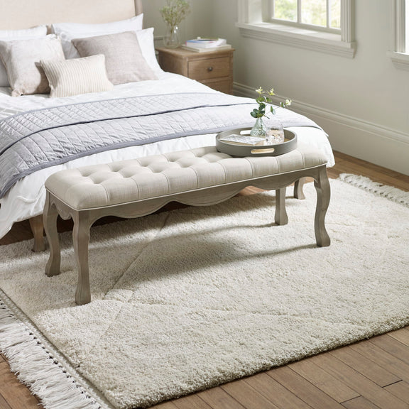 Bedroom with a tufted bench, bed, and rug.