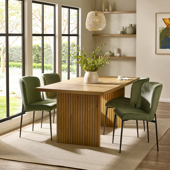 Dining room with wooden table and green chairs near large windows.