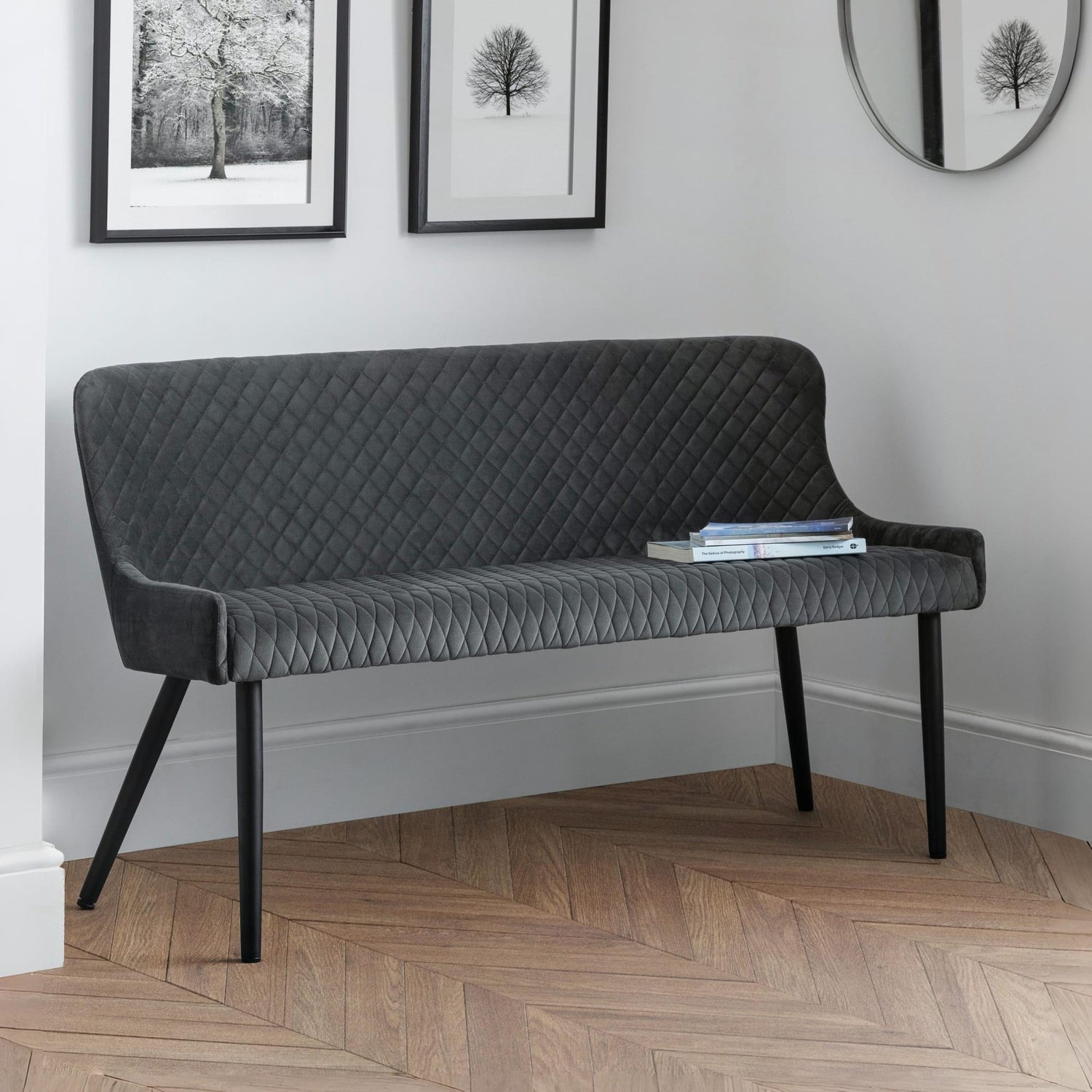 Gray quilted bench in a room with framed pictures on the wall.
