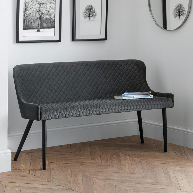 Gray quilted bench in a room with framed pictures on the wall.