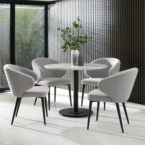 Modern dining set with round table and chairs in a room with large windows.