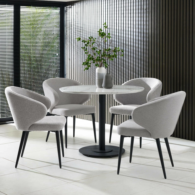 Modern dining set with round table and chairs in a room with large windows.