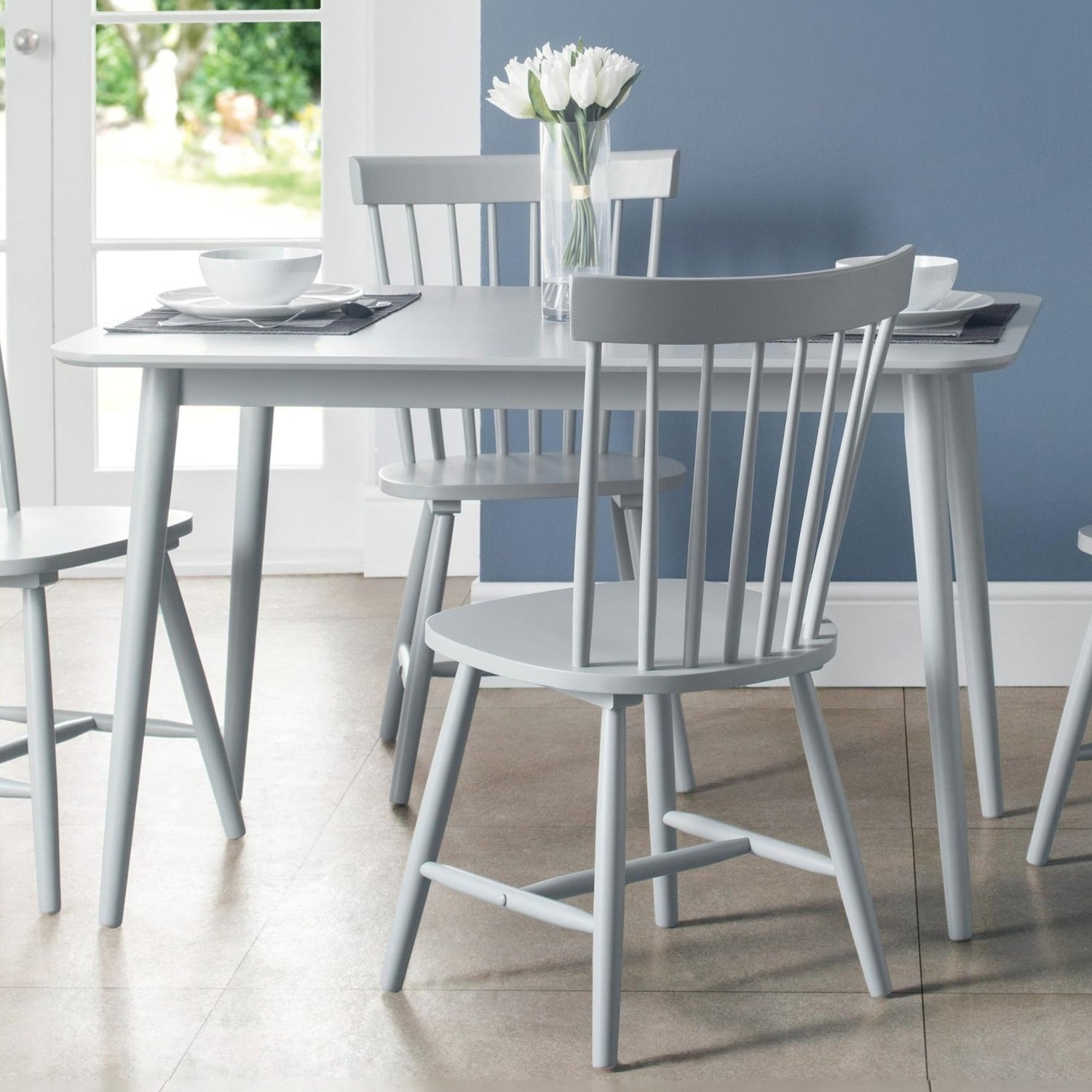 Dining table set with chairs in a room with a blue wall and window.