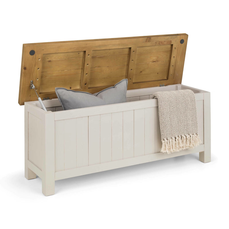 Wooden storage bench with a white interior, containing a gray pillow and beige blanket on a white background.