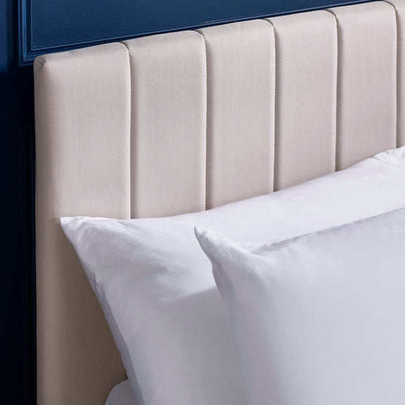 Beige upholstered headboard with white pillows against a dark blue wall.