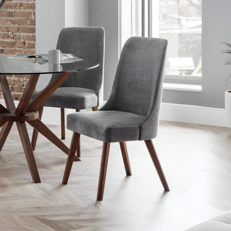 Gray upholstered chairs with wooden legs around a glass dining table in a modern room.