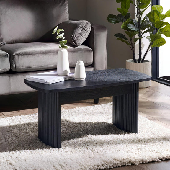 Black coffee table in a living room with a gray sofa and decorative items.