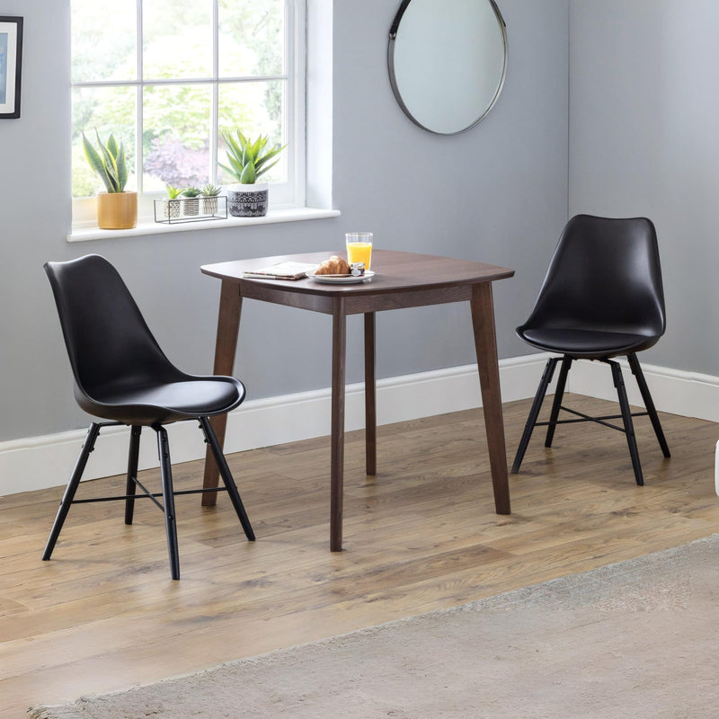 Wooden dining table with two black chairs in a room with a window and plants.