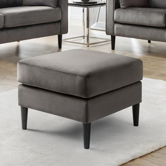 Gray ottoman in a living room setting with gray chairs and a white rug.